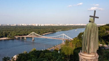 KYIV, UKRAINE - Temmuz. 24, 2021: Kyiv tepelerindeki Aziz Vladimir Anıtı. Yaya köprüsü ve Büyük Vladimir Anıtı ile Dnipro Nehri 'nin manzarası.