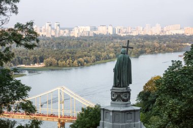 KYIV, UKRAINE - Temmuz. 24, 2021: Kyiv tepelerindeki Aziz Vladimir Anıtı. Yaya köprüsü ve Büyük Vladimir Anıtı ile Dnipro Nehri 'nin manzarası.