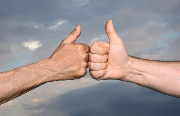 Two men bumping fists with thumbs up against sky with clouds — Stock Photo, Image