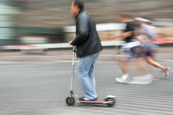 Un bărbat pe un scuter şi o pereche care aleargă pe stradă — Fotografie, imagine de stoc