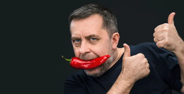 Äldre man med röd paprika i munnen — Stockfoto