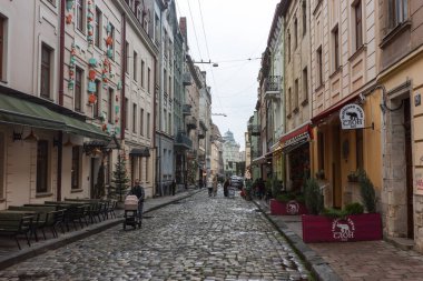 Lviv, Ukrayna - 12 Ekim 2025: Ziyaretçiler Ukrayna 'da bulutlu bir günde yerel dükkanlar, kafeler ve tarihi binaların keyfini çıkararak Lviv kaldırım taşı caddesi boyunca yürüyorlar.
