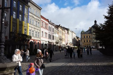 Lviv, Ukrayna - 12 Ekim 2025: İnsanlar Ukrayna 'nın Lviv kentindeki kaldırım taşı caddesinde yürüyor, etrafları parçalı bulutlu bir gökyüzü altında renkli tarihi binalarla çevrili..