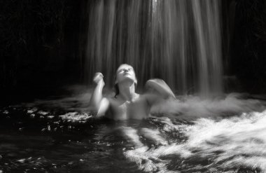Şelalede çıplak poz veren genç bir kadın, şehvetli ve sanatsal bir görüntü yaratıyor.