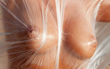 Rüzgarlı deniz sahilinde, plastik ambalajın arkasında güzel, çıplak bir kadın. Polietilen film altında sanatsal vücut portresi, doğa arka planı. Kavramsal açık hava fotoğrafı.