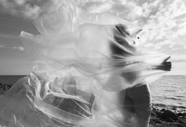 Rüzgarlı deniz sahilinde, plastik ambalajın arkasında güzel, çıplak bir kadın. Polietilen film altında sanatsal vücut portresi, doğa arka planı. Kavramsal açık hava fotoğrafı.