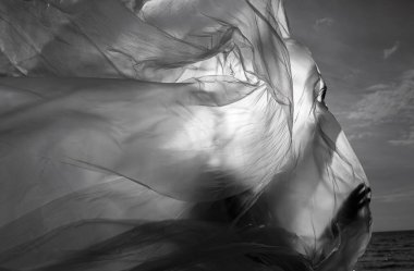 Rüzgarlı deniz sahilinde, plastik ambalajın arkasında güzel, çıplak bir kadın. Polietilen film altında sanatsal vücut portresi, doğa arka planı. Kavramsal açık hava fotoğrafı.