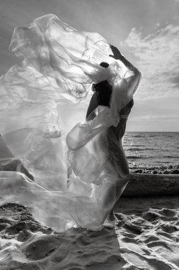 Rüzgarlı deniz sahilinde, plastik ambalajın arkasında güzel, çıplak bir kadın. Polietilen film altında sanatsal vücut portresi, doğa arka planı. Kavramsal açık hava fotoğrafı.