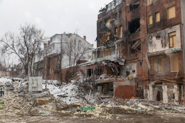 Harkiv 'de yıkılan bir konut binasında çökmüş tuğla bir cephe ve kırılmış camlar bulunuyor. İtfaiyeciler, karla kaplı molozların üzerindeki yıkık bir balkonda çalışıyorlar..