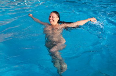 Yüzme havuzunda çıplak bir kadın. Genç çıplak bir kadın havuzda açık havada yüzüyor. Mavi suda kollarını hareket ettirirken kadın gülümsüyor..