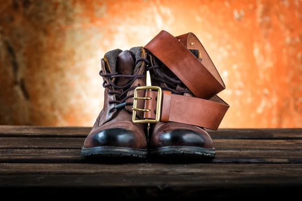 Brown winter boots and leather belt with buckle, wooden background