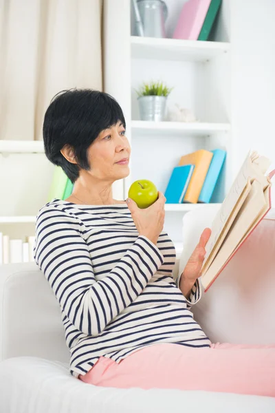 Azjatycki dojrzała kobieta starszy czytanie na kanapie — Zdjęcie stockowe