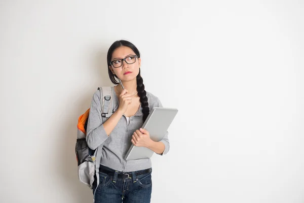 Asian college girl thinking holding a pen with laptop on plain b — Stock Photo, Image