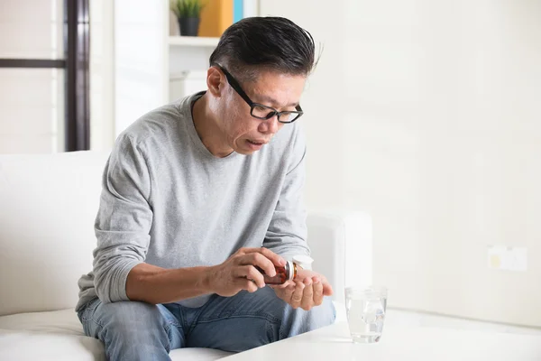 Старший азиатский человек, принимающий таблетки — стоковое фото