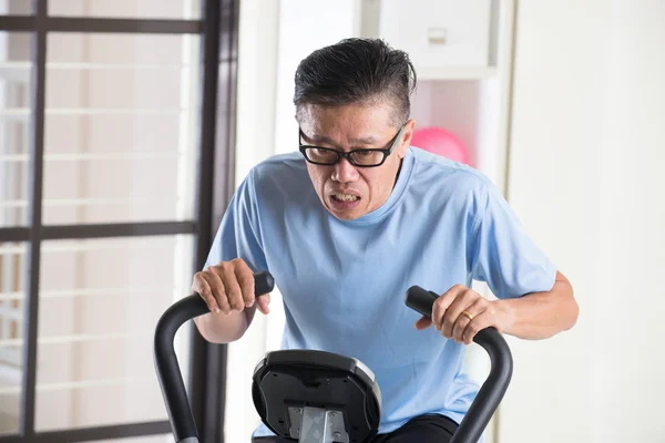 Cansado asiático senior macho en bicicleta estática —  Fotos de Stock