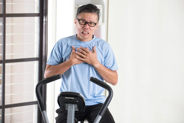 Asian senior male on exercise bike — Stock Photo, Image