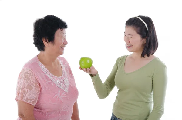 Eldre kvinne med datter som får eple – stockfoto