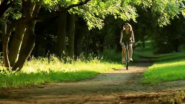 Donna che inizia ad andare in bicicletta attraverso un parco di erba verde sugli alberi e il tramonto — Video Stock