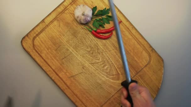 Mãos masculinas afiando uma faca contra um fundo de uma placa de cozinha de madeira velha — Vídeo de Stock