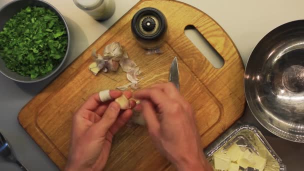 Mannelijke handen pellen en snijden van knoflook op een houten plank van koken — Stockvideo