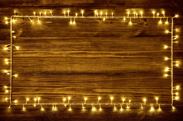Luces de guirnalda sobre fondo de madera, marco de madera de vacaciones, tablones marrones —  Fotos de Stock