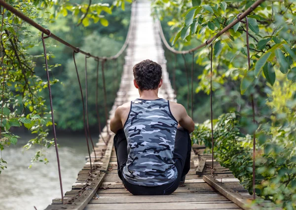 Bir köprü üzerinde oturan genç çocuk — Stok fotoğraf