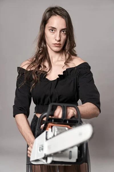 Scary young woman holding a chainsaw with a menacing expression