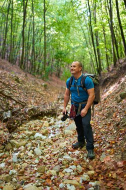 Profesyonel doğa fotoğrafçısı, kamera ve büyük sırt çantasıyla ormanda geziniyor.