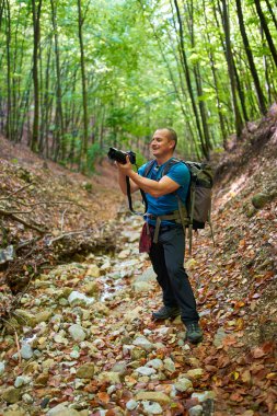 Profesyonel doğa fotoğrafçısı, kamera ve büyük sırt çantasıyla ormanda geziniyor.