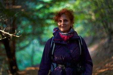 Kameralı ve sırt çantalı doğa fotoğrafçısı kadın ormana doğru yürüyor.