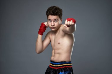 Gri arka planda boks eğitimi almış genç kickboksçu.