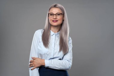 Gözlüklü genç iş kadını, kollarını kavuşturmuş, gri arka planda yakın plan.