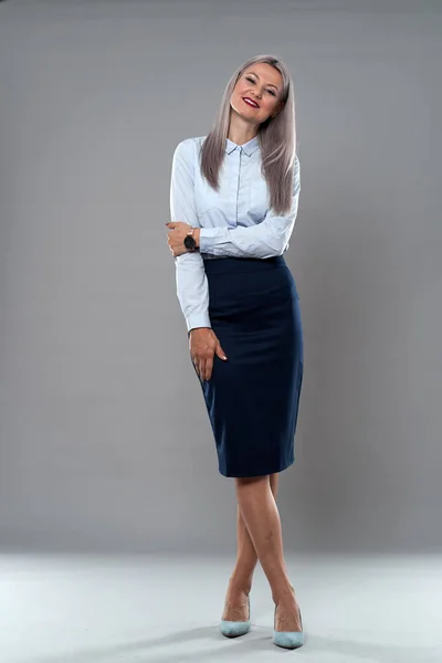 Successful businesswoman in formal attire, full length studio shot against gray background