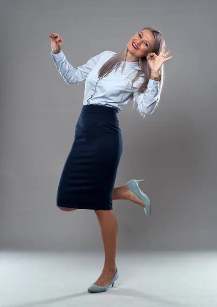 Successful businesswoman in formal attire, full length studio shot against gray background