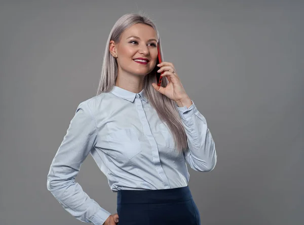 若い実業家は彼女の携帯電話で話すグレーの背景 — ストック写真