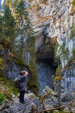 Ağır sırt çantalı, tripodlu ve kameralı profesyonel doğa fotoğrafçısı büyük bir mağaranın girişinde çekim yapıyor.