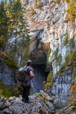 Ağır sırt çantalı, tripodlu ve kameralı profesyonel doğa fotoğrafçısı büyük bir mağaranın girişinde çekim yapıyor.