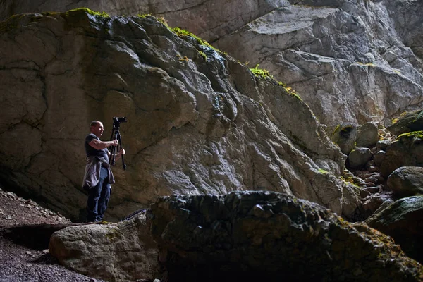 洞窟の中に大きなバックパック 三脚やカメラを持つプロの写真家 — ストック写真