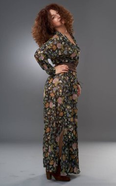 50 yaşında güzellik. Uzun elbiseli, kıvırcık saçlı olgun bir kadının stüdyo portresi.