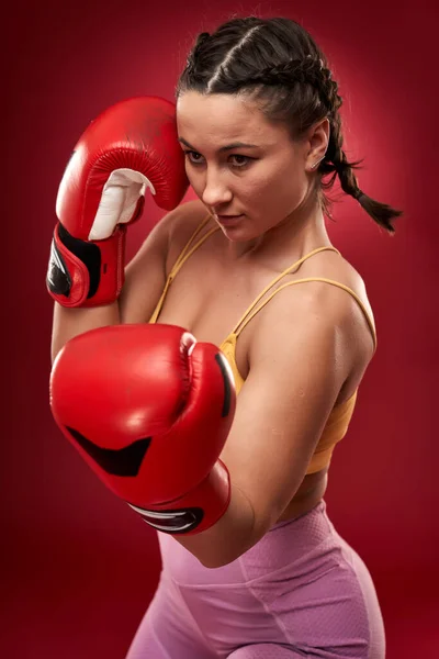 Young female boxer with red gloves on red background