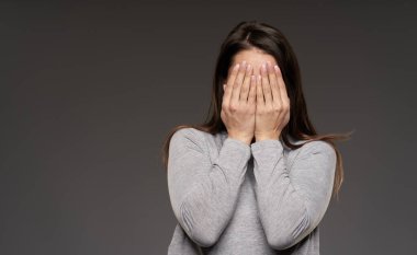 Yüzünü elleriyle kapatan kadın. Gri arka planda telif alanı var.