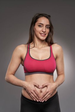 Spor pantolonu ve gri arka planda sutyen giyen aktif hamile bir kadın.