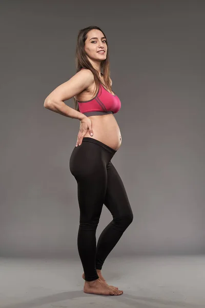 アクティブ妊娠中の女性でスポーツパンツとブラ上のグレーの背景 — ストック写真