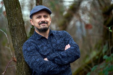 Meyve bahçesindeki bir ağaca yaslanmış orta yaşlı bir çiftçinin yakın çekimi.