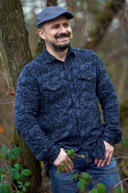 Meyve bahçesindeki bir ağaca yaslanmış orta yaşlı bir çiftçinin yakın çekimi.