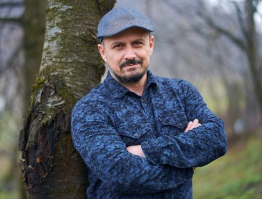 Meyve bahçesindeki bir ağaca yaslanmış orta yaşlı bir çiftçinin yakın çekimi.