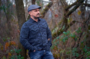 Meyve bahçesindeki bir ağaca yaslanmış orta yaşlı bir çiftçinin yakın çekimi.