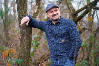 Meyve bahçesindeki bir ağaca yaslanmış orta yaşlı bir çiftçinin yakın çekimi.