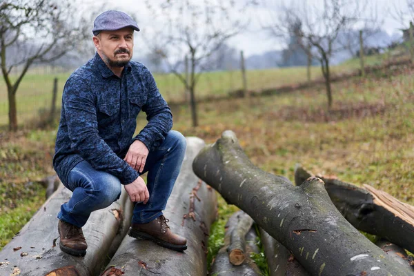 Agricultor Calça Azul Camisa Boné Sentado Uma Pilha Troncos Para — Fotografia de Stock