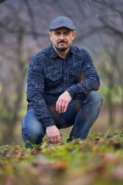 Kot pantolonlu ve kepli çiftçi kış başında meyve bahçesinde poz veriyor.